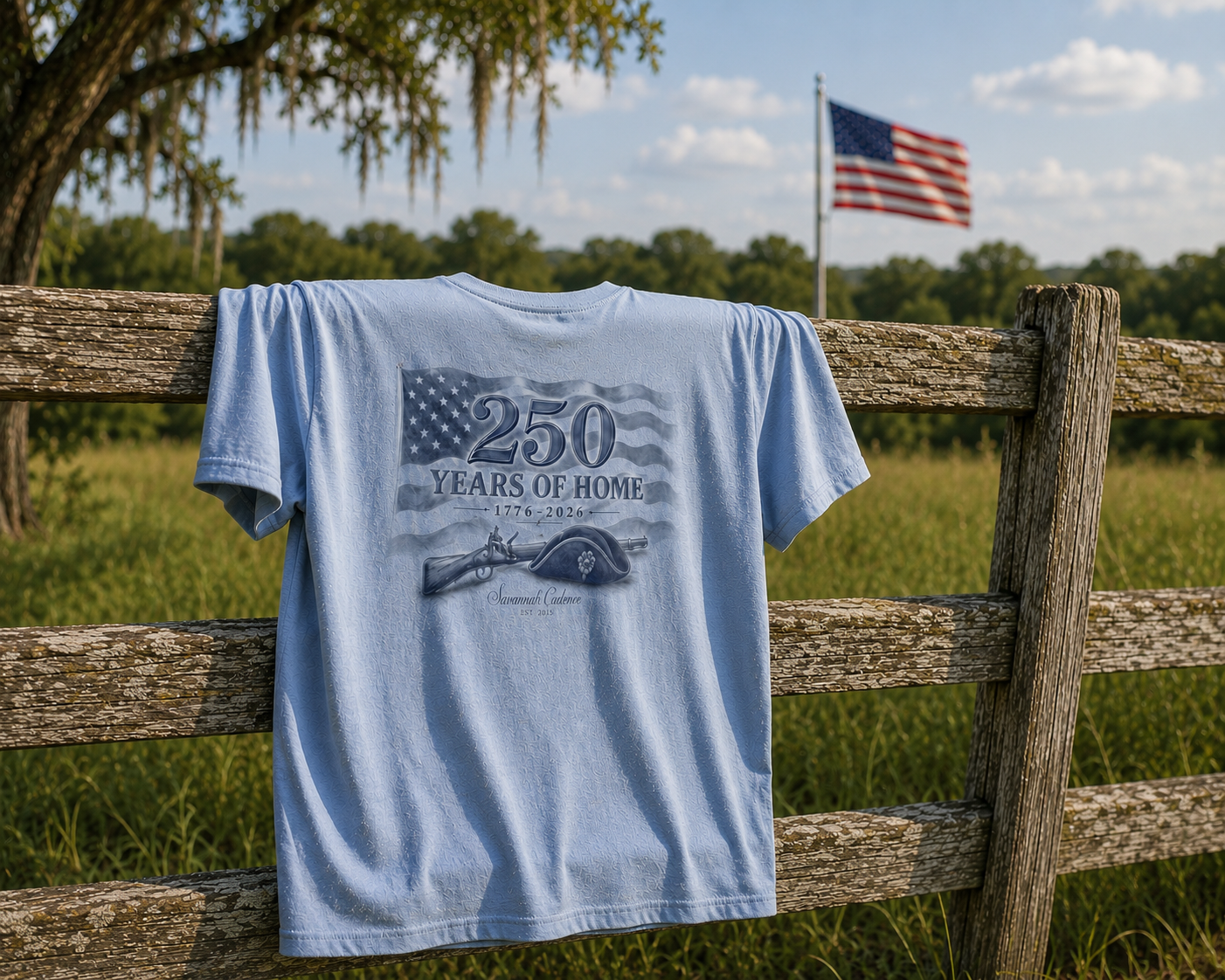 Savannah Cadence 250 Years of Home Tee hanging on a split-rail fence with an American flag in the background