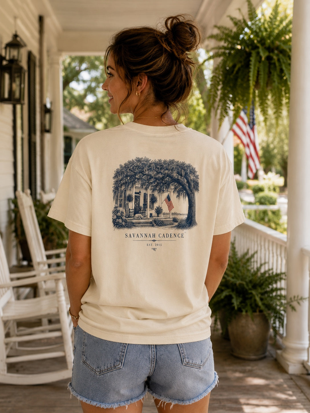 Woman wearing the Savannah Cadence Front Porch Tee on a Southern front porch featuring vintage porch artwork beneath a live oak.